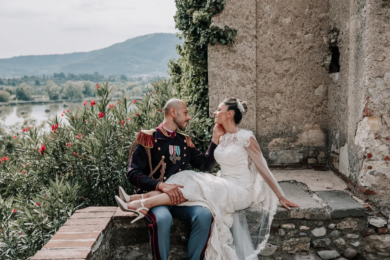 Giulia e Giovanni, lui in alta uniforme, seduti su un muretto in pietra tra gli oleandri, con il lago d’Iseo sullo sfondo