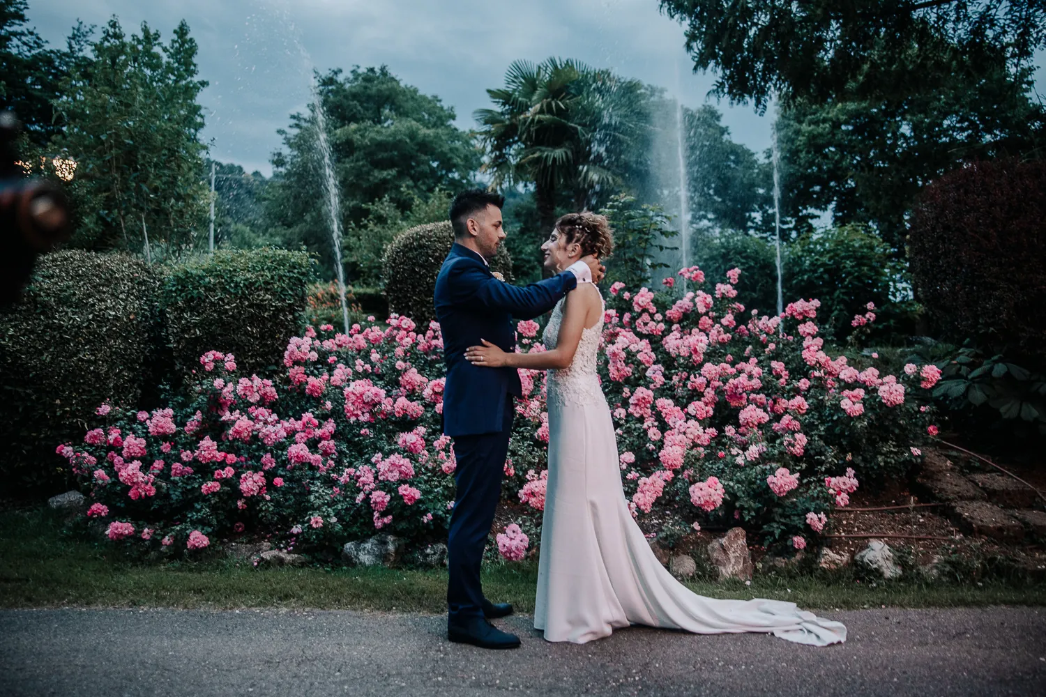 Luca e Ilaria abbracciati davanti alle rose rosa del parco di Casa Mascagni, con le fontane e le palme sullo sfondo