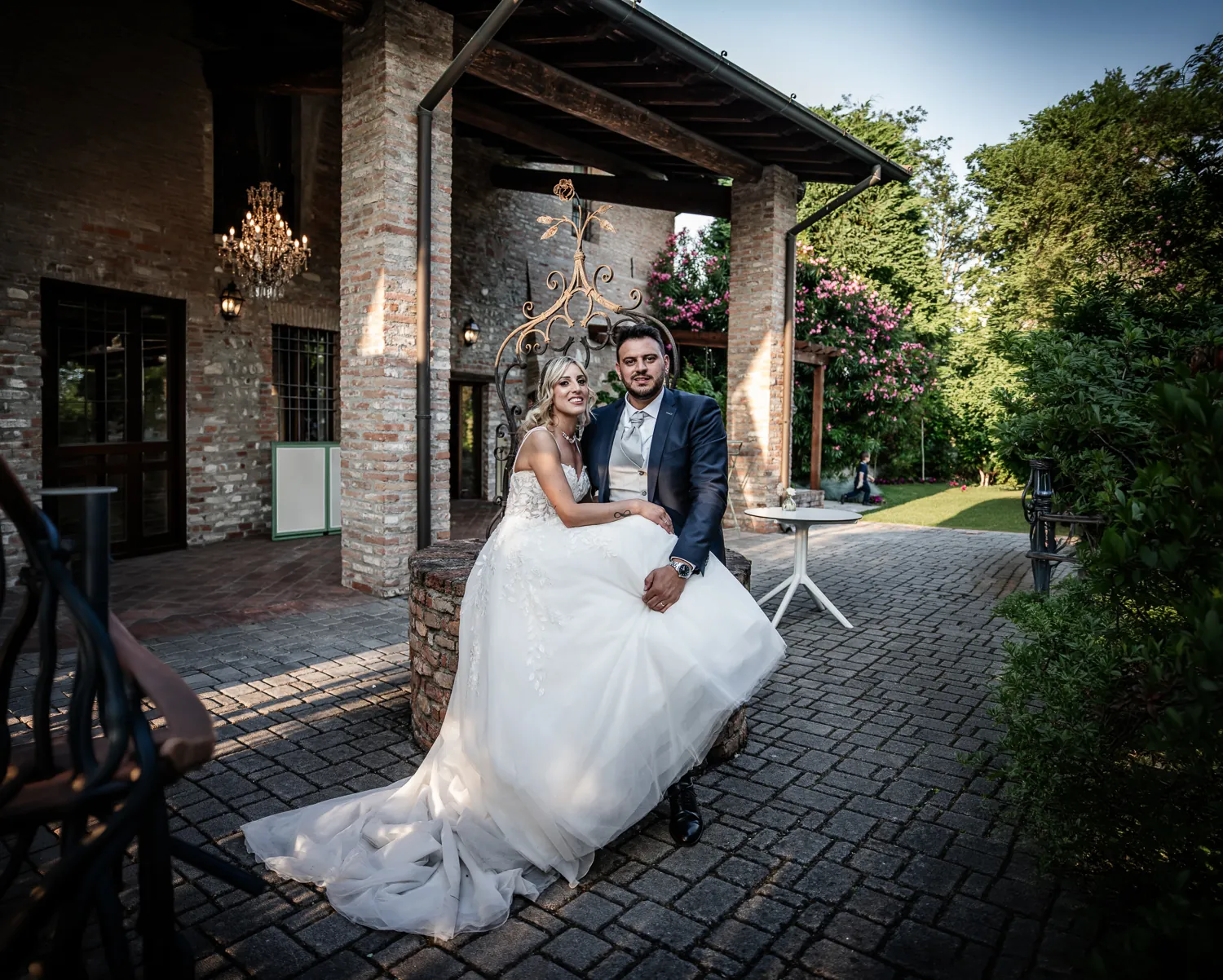 Andrea e Michelle seduti sotto il portico in mattoni di Corte Piovanelli, con il lampadario di cristallo e il giardino alle spalle